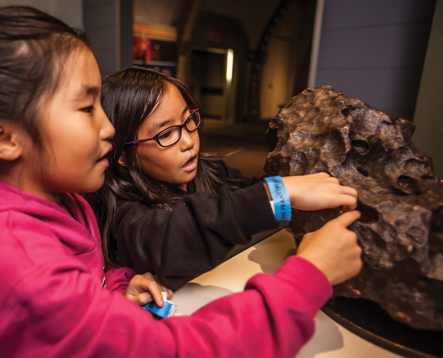Two young girls touching the meteorite in the Space Command permanent exhibit at The Franklin Institute.