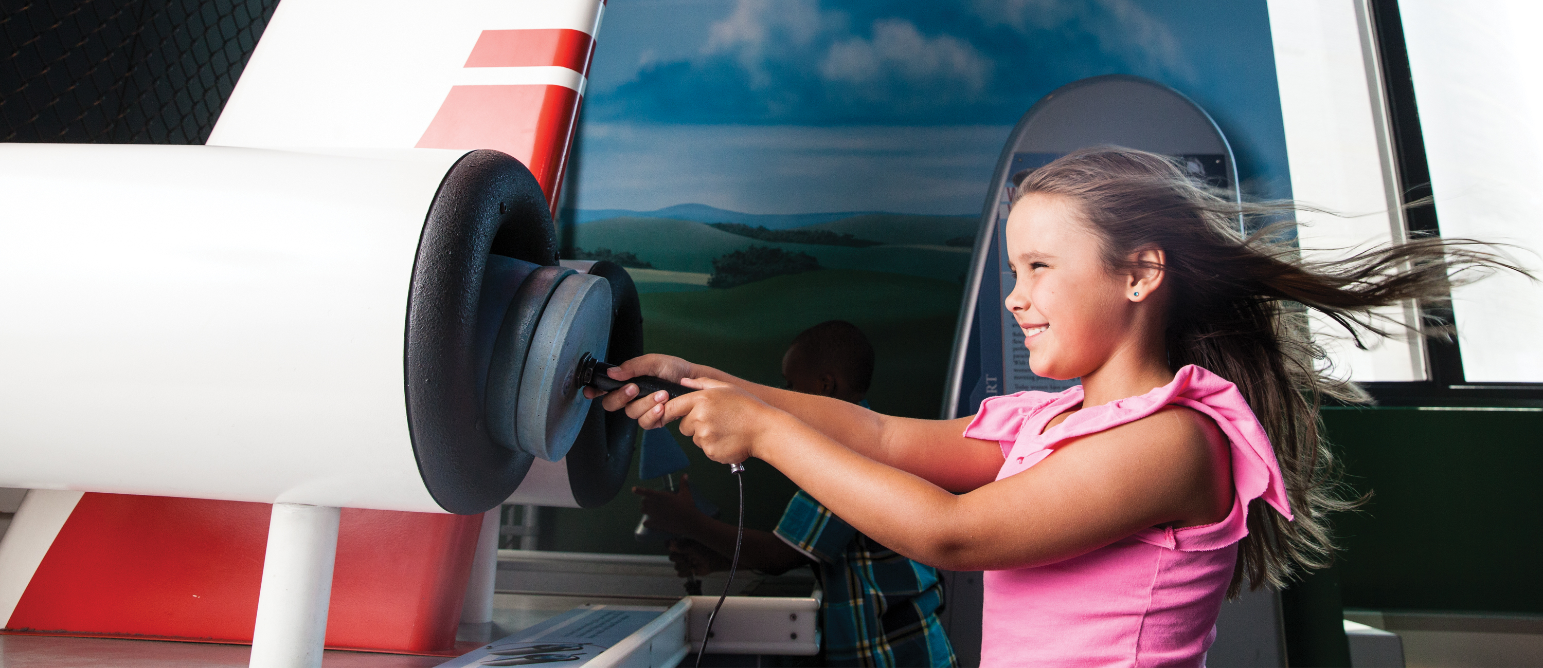 A young girl is playing with and learning from an interactive about wind, in the Franklin Insitute's permanent exhibit, Franklin Air Show.