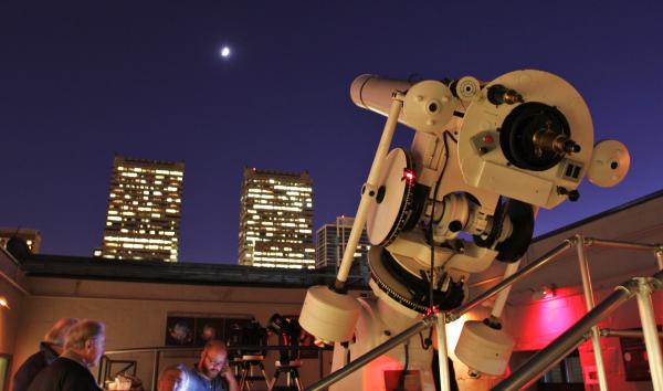 telescope pointing up to a star in the sky at night with people in background