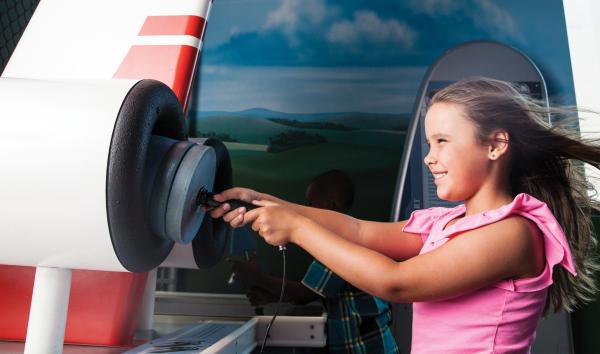 A young girl is playing with and learning from an interactive about wind, in the Franklin Insitute's permanent exhibit, Franklin Air Show.