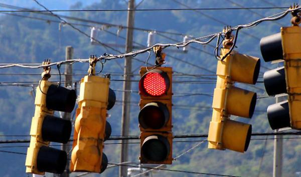 Several traffic lights hang from wires over a street in a mountainous area.