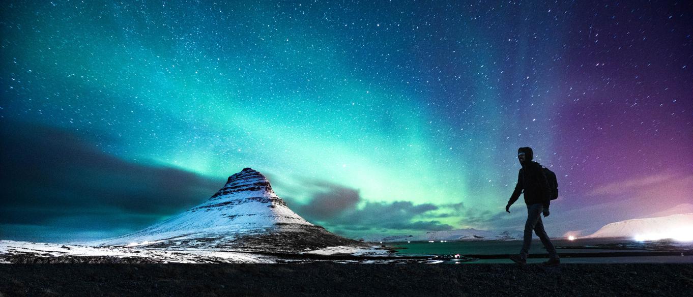 A hiker silhouetted in front of the Northern Lights in Mount Kirkjufell, Iceland.