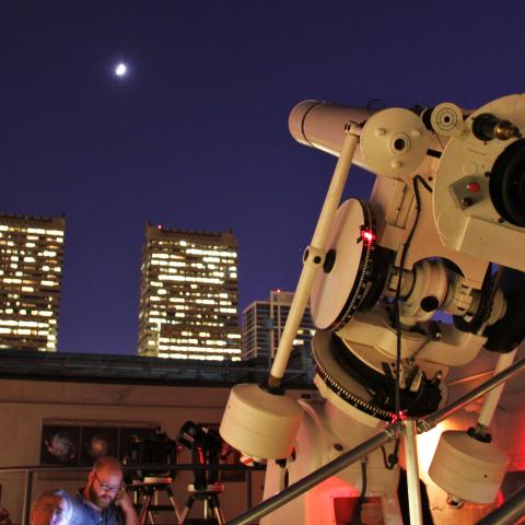 telescope pointing up to a star in the sky at night with people in background