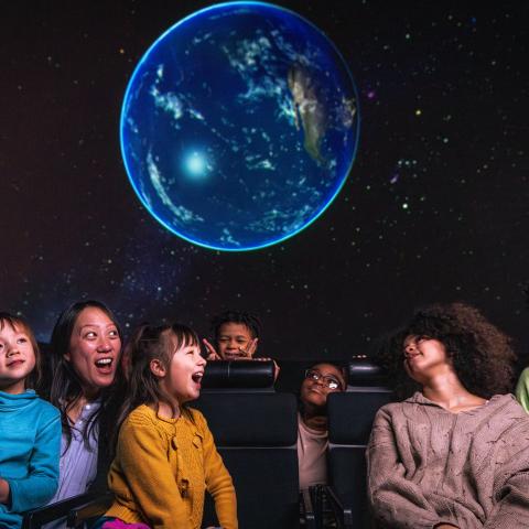 Joyful families seated in the planetarium, beneath the starfield.